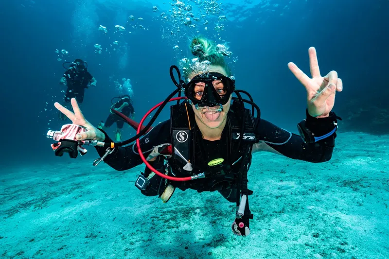 Plongeuse souriante fait signe de la main sous l'eau en mer