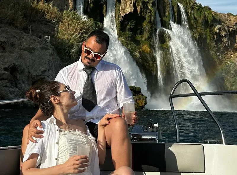 Couple souriant sur un bateau devant une cascade spectaculaire