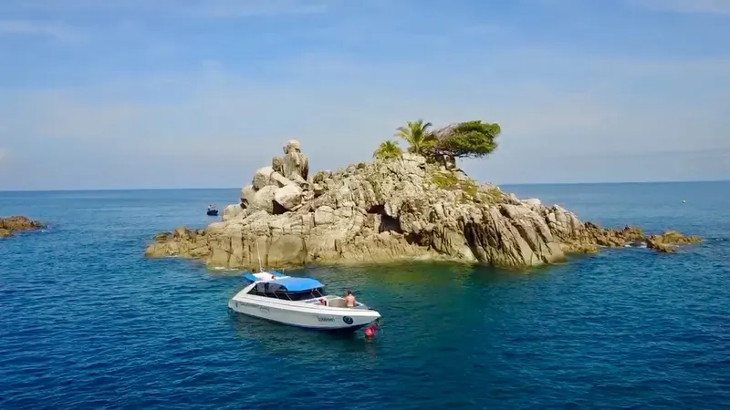 Bateau de plaisance navigue près d'une île rocheuse sous ciel bleu