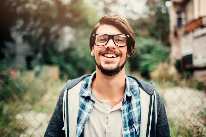 Jeune homme souriant, portant des lunettes et une chemise à carreaux