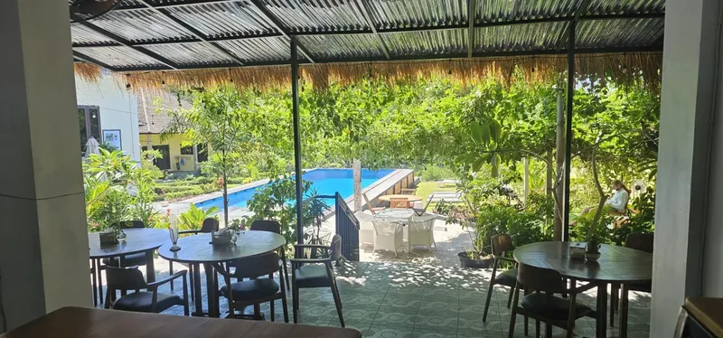 Terrasse ombragée avec tables, chaises et végétation luxuriante en arrière-plan