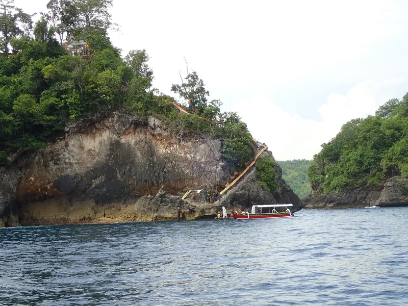Bateau de plongée amarré devant une falaise verdoyante et rocheuse