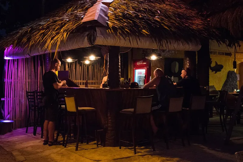 Bar de plage ouvert le soir avec quelques clients assis au comptoir
