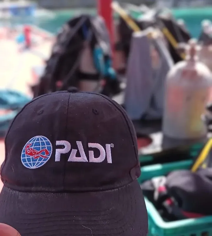 Casquette PADI bleue avec logo, équipement de plongée en arrière-plan