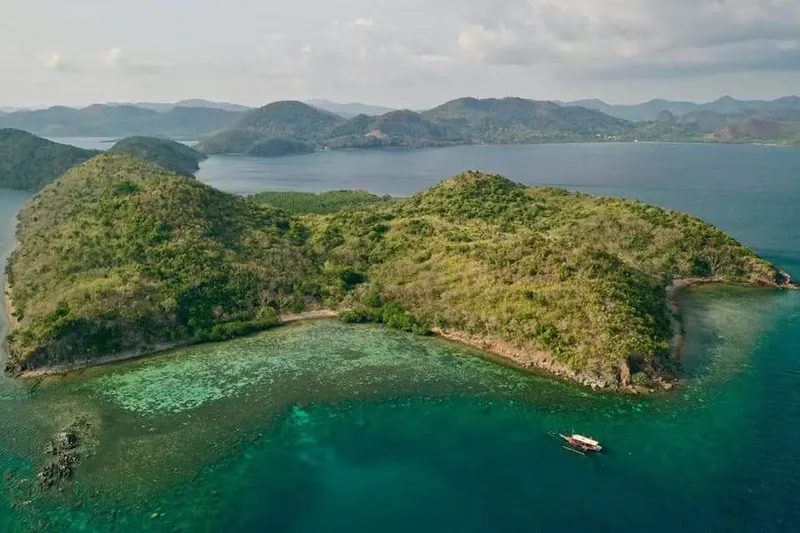 Île tropicale luxuriante entourée d'eaux turquoise et d'un bateau traditionnel