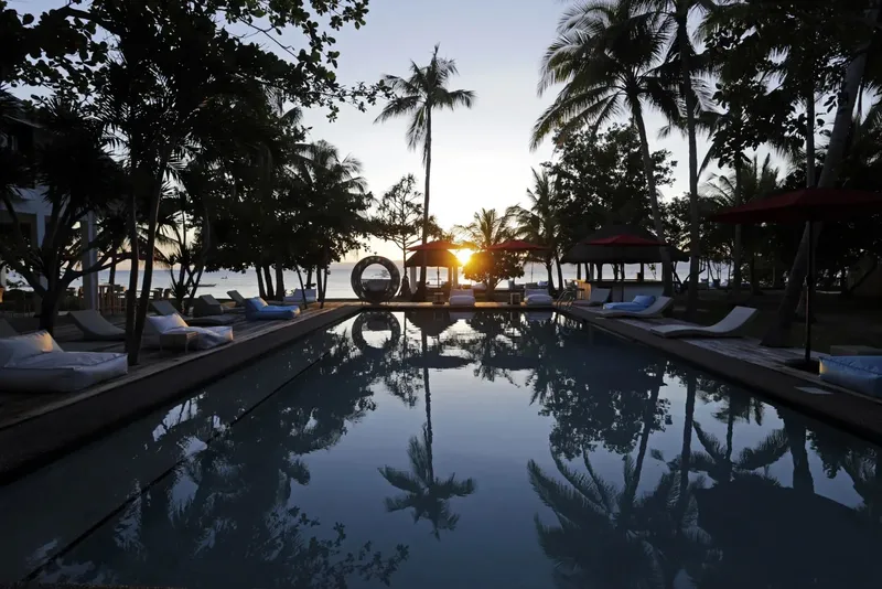 Piscine avec transats et palmiers au coucher du soleil