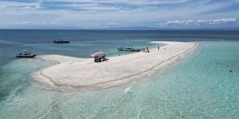 Îlot de sable blanc avec quelques personnes et bateaux en mer