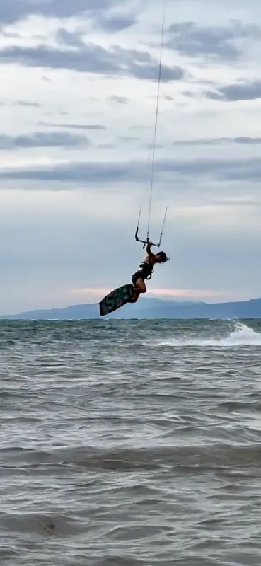 Kitesurfeur en plein saut au-dessus de l'eau, ciel nuageux en arrière-plan