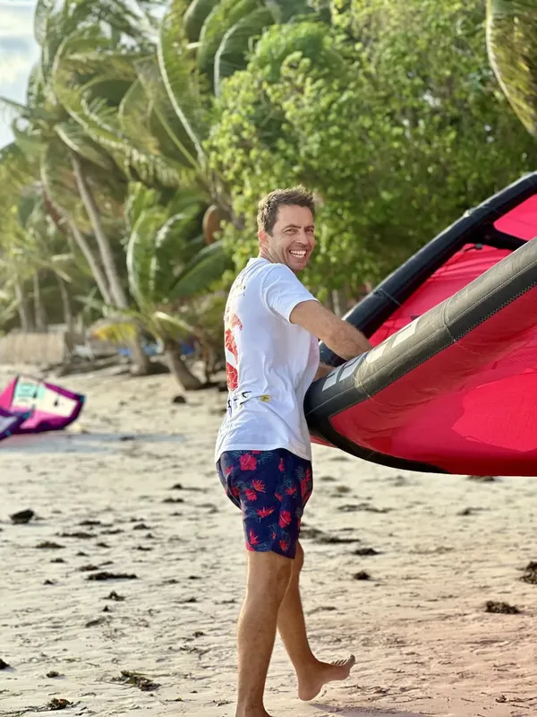 Un homme souriant marche sur la plage avec une voile rouge