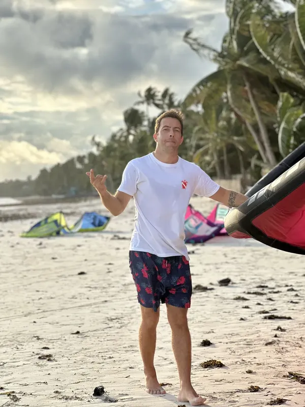 Un homme sur une plage de sable, avec des planches de kitesurf