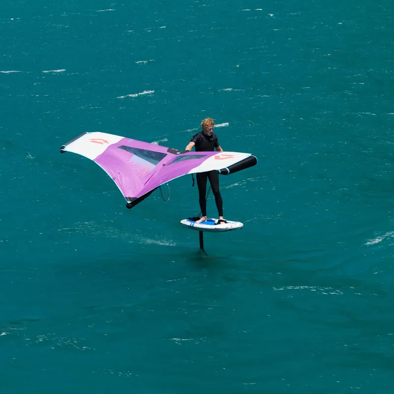 Une personne pratique le wingsurf sur une mer turquoise calme
