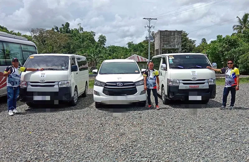 Trois personnes posent devant des fourgonnettes blanches sur gravier