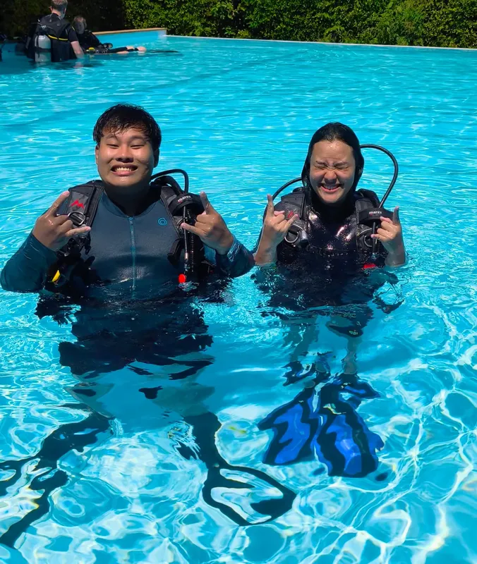 Deux plongeurs souriants en combinaison dans une piscine bleu clair