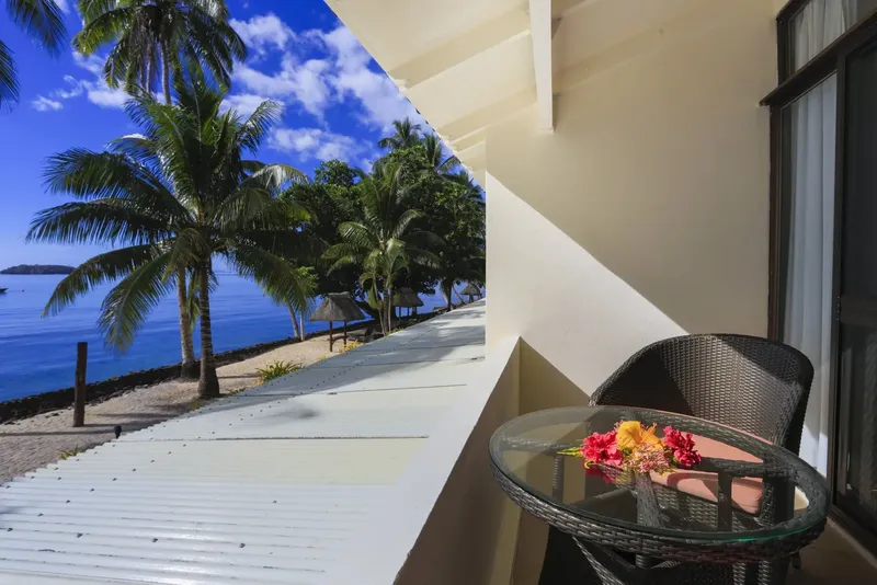 Vue d'une terrasse avec mobilier, mer turquoise et palmiers au loin