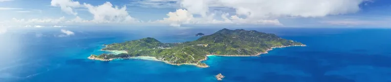 Vue aérienne d'une île tropicale entourée d'eau turquoise et de nuages