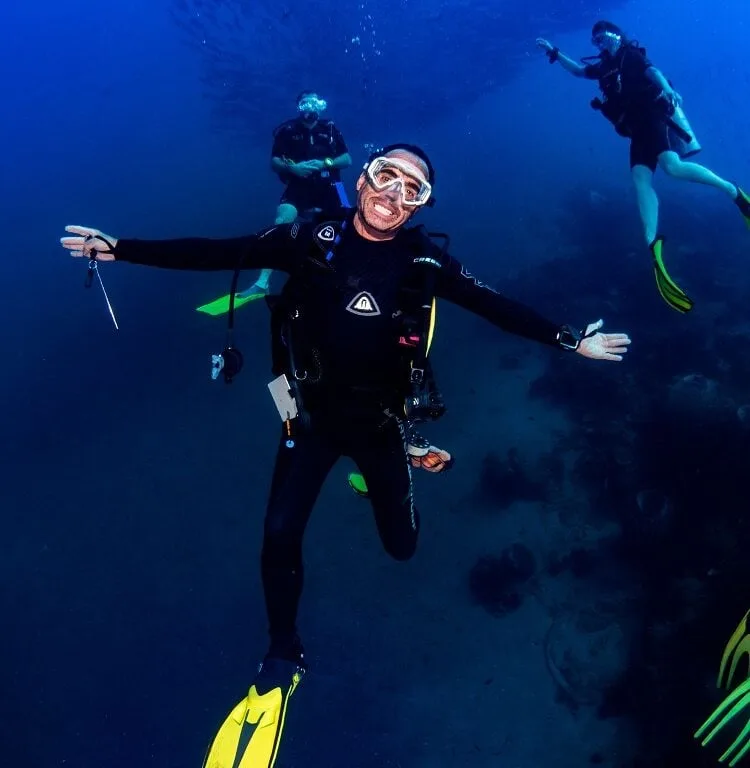 Trois plongeurs souriants évoluent dans une eau bleue claire