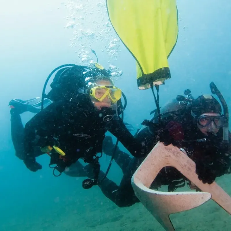 Deux plongeurs en combinaison scrutent le fond marin bleu turquoise