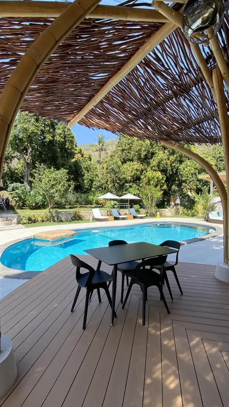 Terrasse ombragée avec table et chaises, piscine et végétation luxuriante