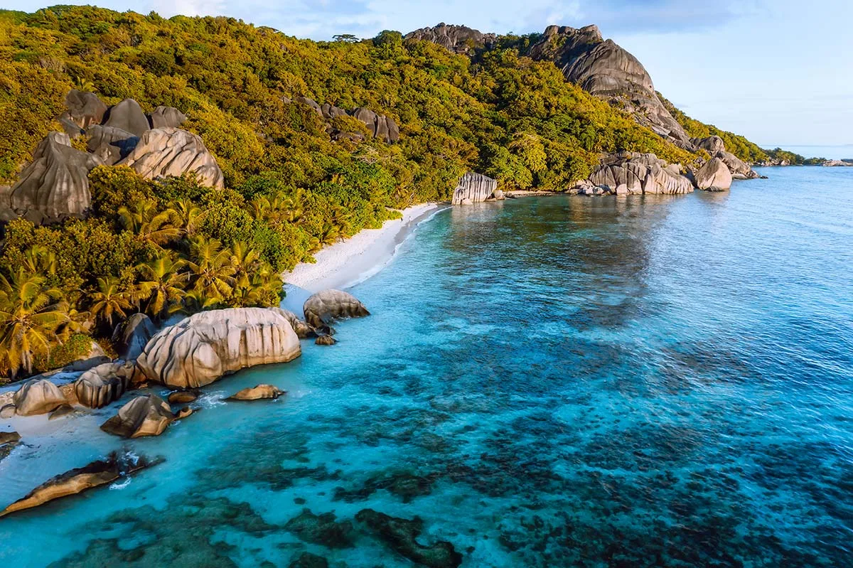 Plage de sable blanc, eau turquoise, végétation luxuriante et rochers de granit