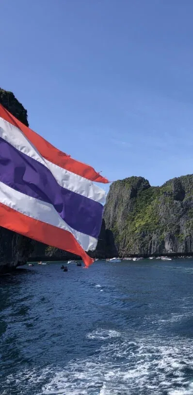 Drapeau thaïlandais flottant au vent, devant une côte rocheuse et des bateaux