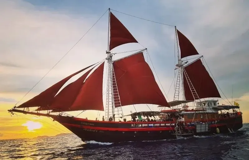 Grand voilier rouge en mer avec des passagers au coucher du soleil