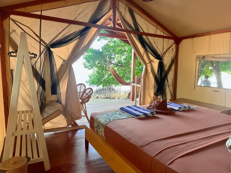Intérieur d'une tente aménagée en chambre avec lit et vue sur mer