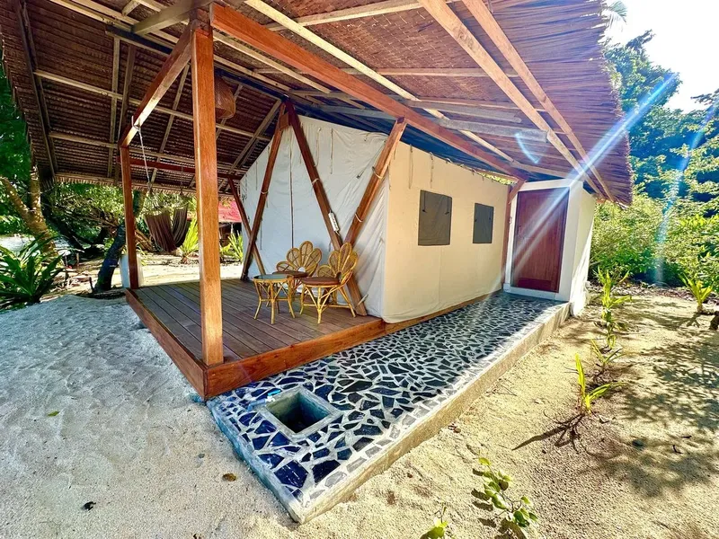 Tente de plage sur sable blanc avec terrasse en bois et végétation