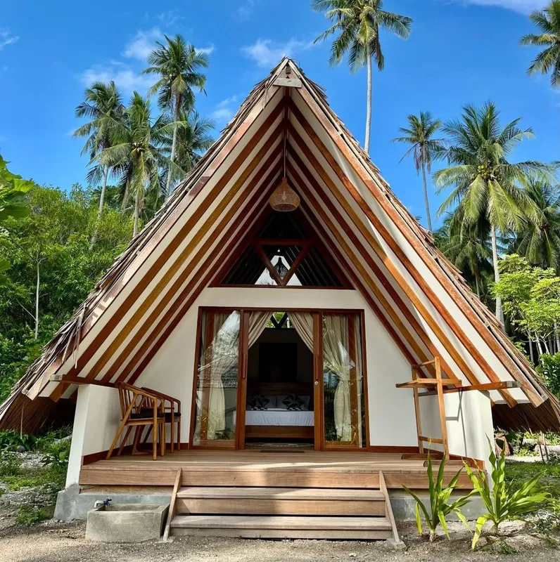 Maison en bois triangulaire avec terrasse, entourée de végétation tropicale