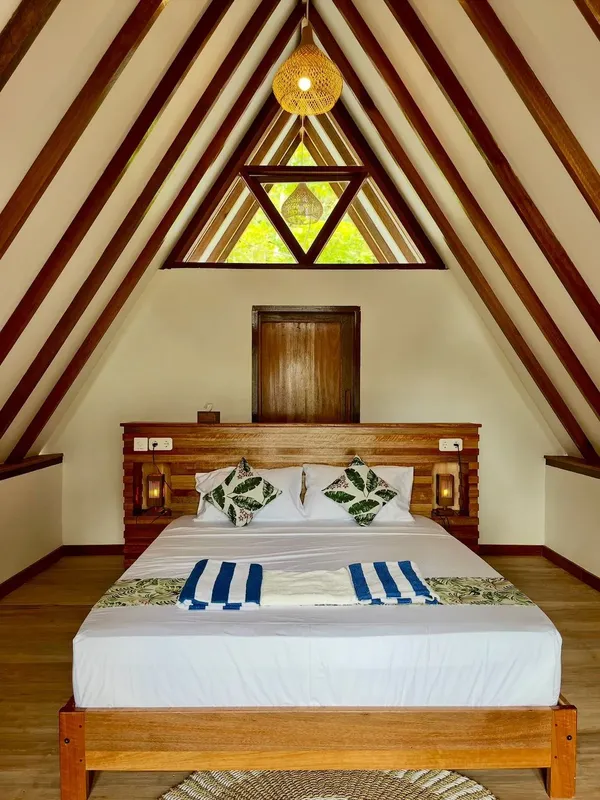 Chambre avec lit double, décoration tropicale, fenêtre triangulaire et éclairage chaleureux