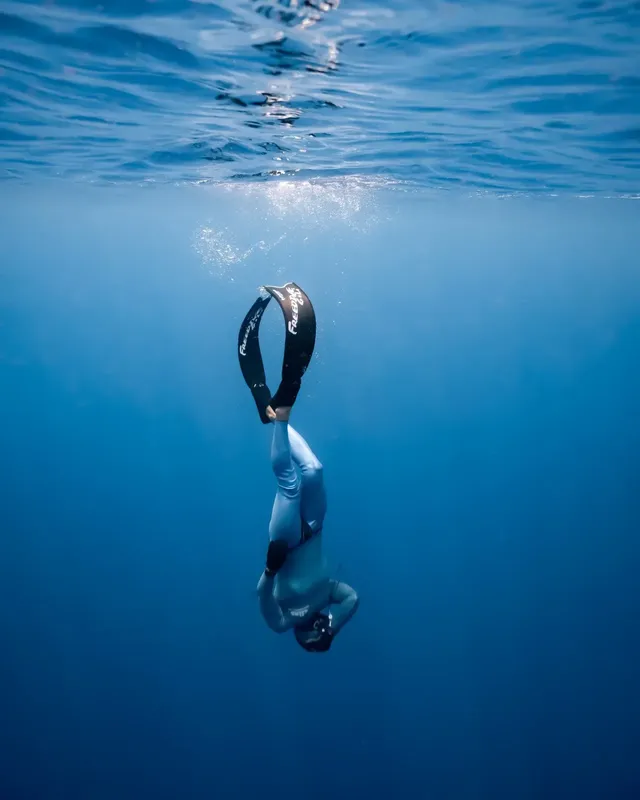Apnéiste en combinaison descend verticalement dans une eau bleu clair