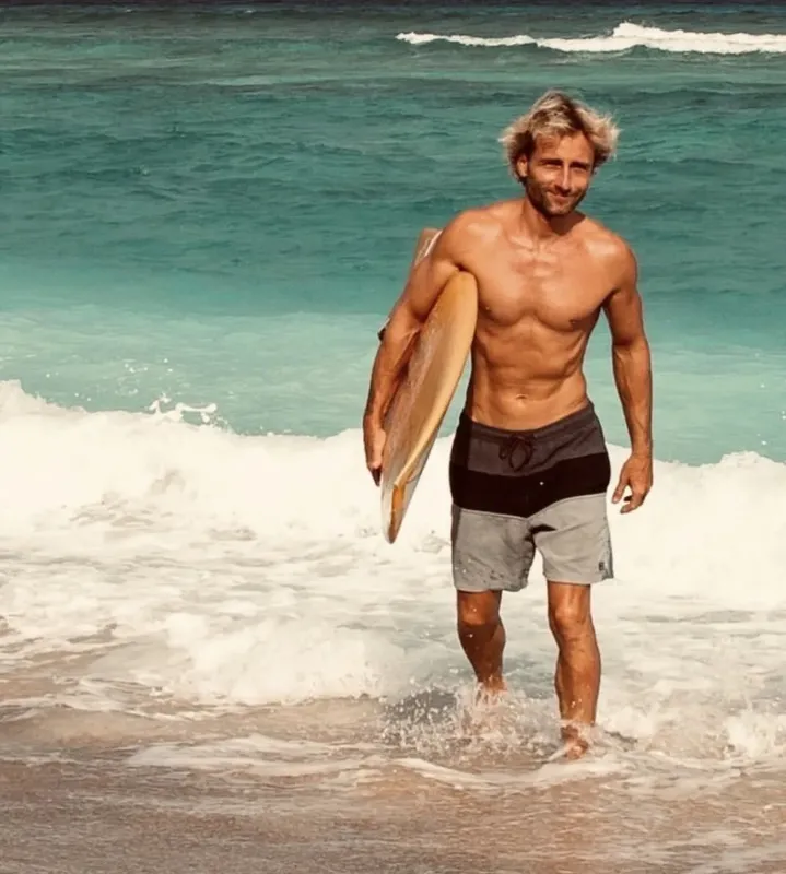 Un homme souriant sort de l'eau avec une planche de surf