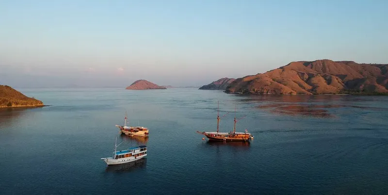 Trois bateaux traditionnels naviguent sur une mer calme au coucher du soleil