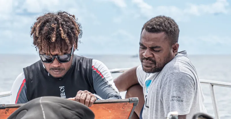 Deux hommes regardent attentivement une carte ou un plan sur un bateau