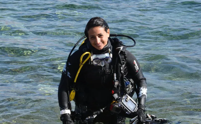 Plongeuse souriante en combinaison, masque et détendeur dans l'eau