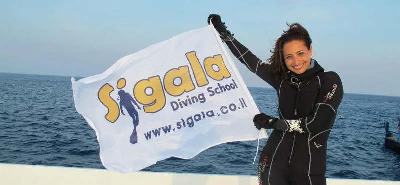 Plongeuse souriante tenant un drapeau avec le nom d'une école