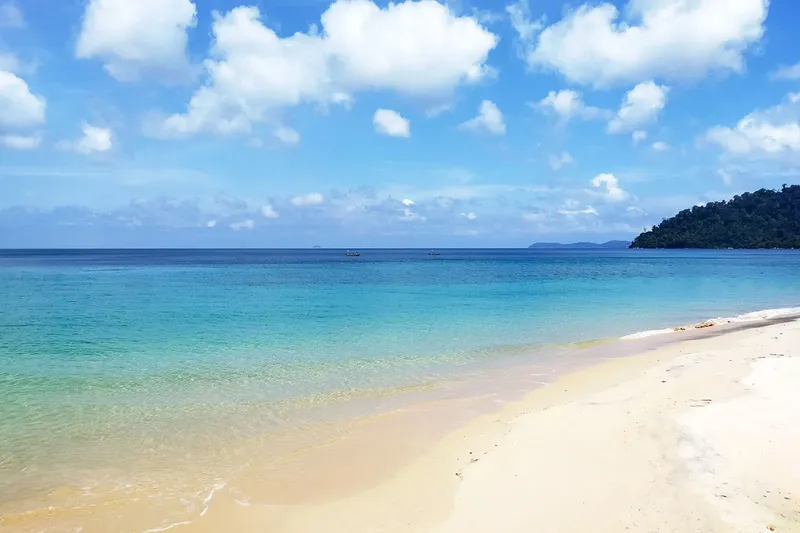 Plage de sable blanc, mer turquoise et quelques bateaux au loin