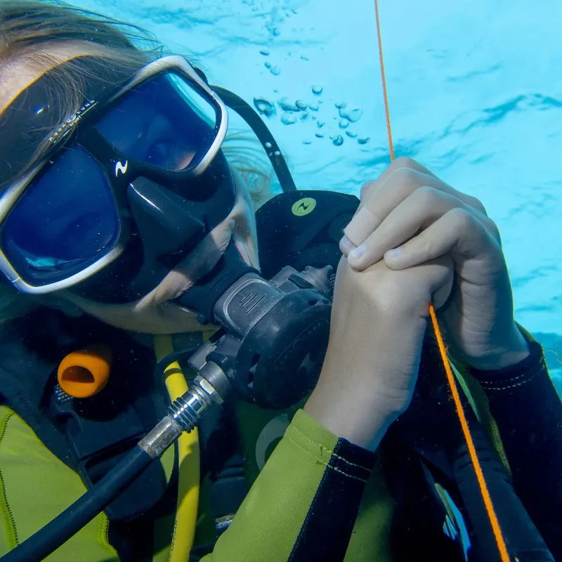 Plongeuse vérifiant son détendeur sous l'eau, équipement complet visible