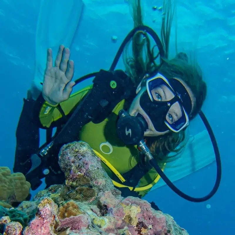 Plongeuse souriante avec combinaison et masque, main levée sous l'eau