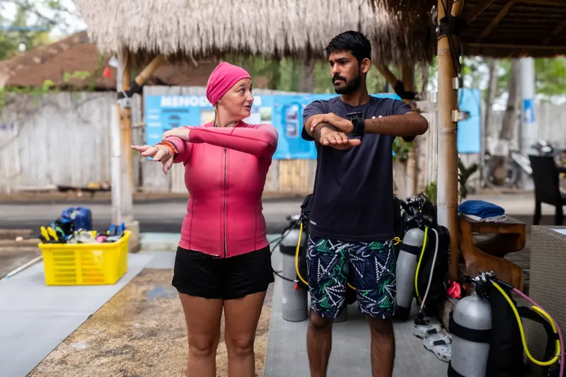 Deux personnes discutent, équipement de plongée en arrière-plan, ambiance tropicale