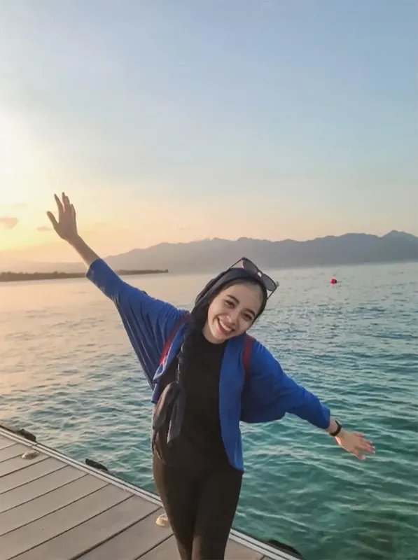Jeune femme souriante bras ouverts sur un ponton au coucher du soleil