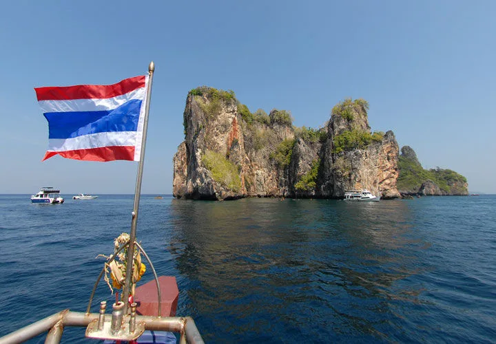 Drapeau thaïlandais flottant devant une île rocheuse en mer