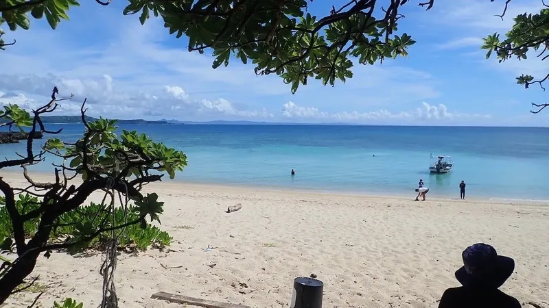 Plage de sable clair avec des personnes et un bateau en mer