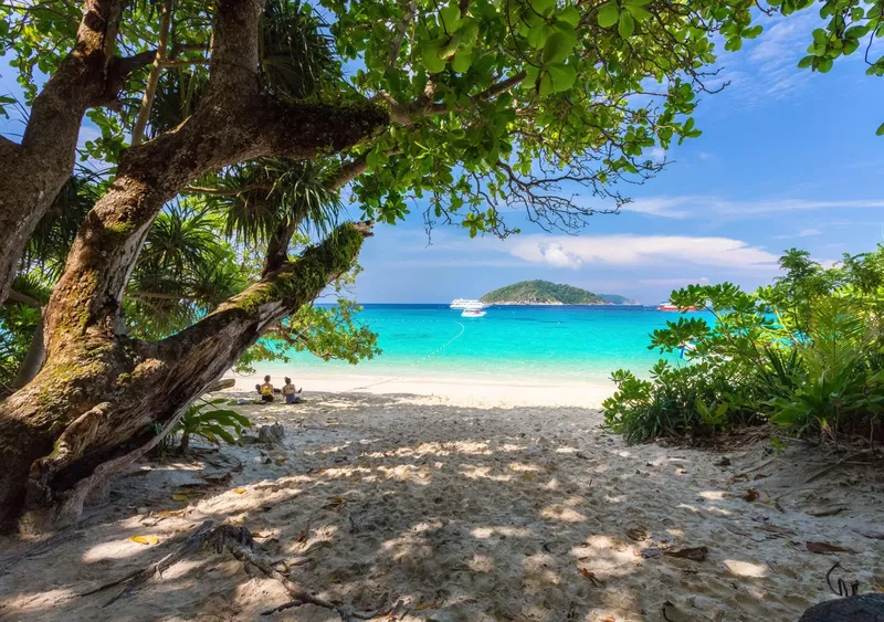 Plage de sable blanc avec des personnes assises et bateaux en mer