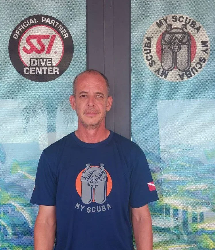 Homme souriant devant une facade avec logos de centre de plongée