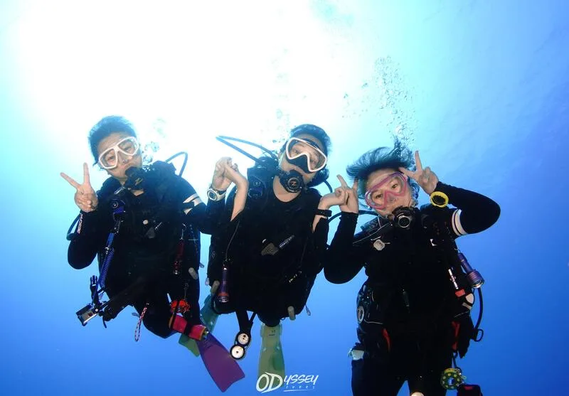 Trois plongeurs souriants font des signes de la main sous l'eau