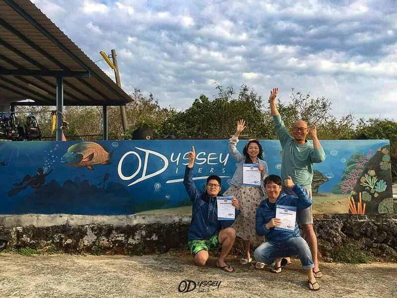 Groupe de plongeurs souriants posant avec leurs certificats devant une fresque