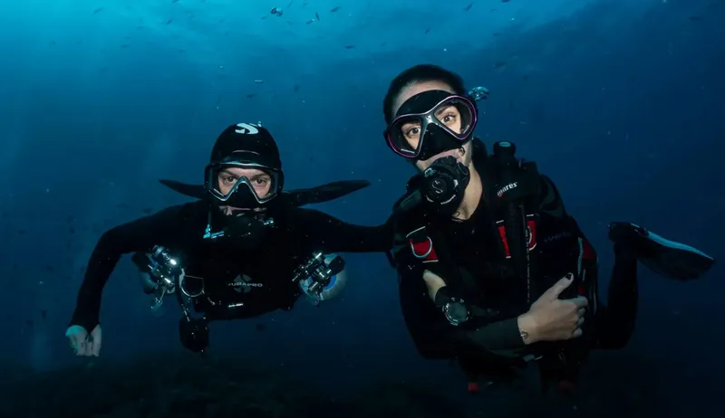 Deux plongeurs souriants en combinaison, équipés, flottent dans l'eau bleue