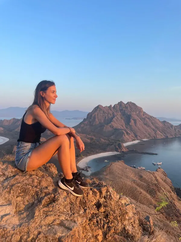 Jeune femme assise sur une roche, vue sur la mer et montagnes