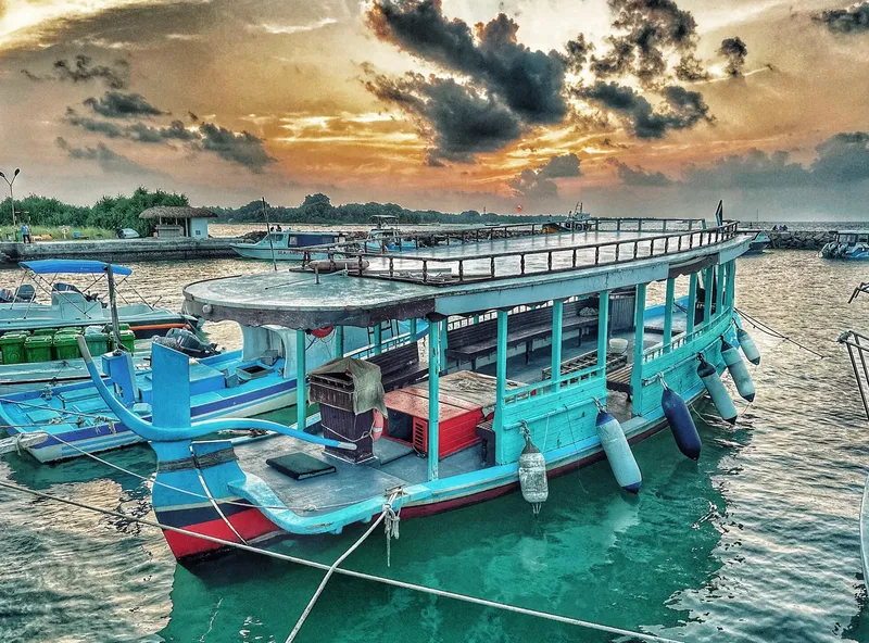 Bateau de plongée turquoise amarré au ponton sous un ciel nuageux