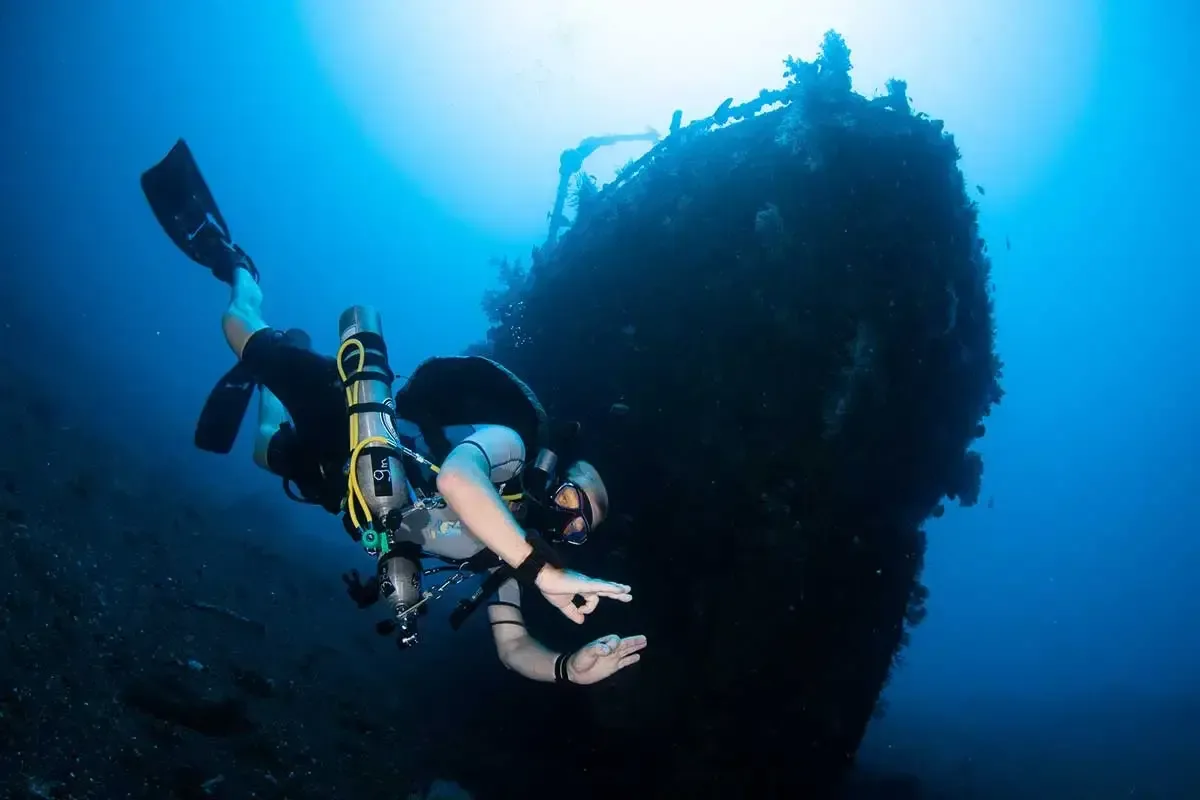 Plongeur explore une épave sombre dans l'eau bleue